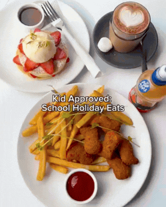 A child's meal with a plate of chicken tenders, French fries, and sliced strawberries with a dollop of ketchup, alongside a cup of chocolate milk, a hot chocolate with whipped cream and heart-shaped foam art, a small bottle of syrup, and a cup of coffee.