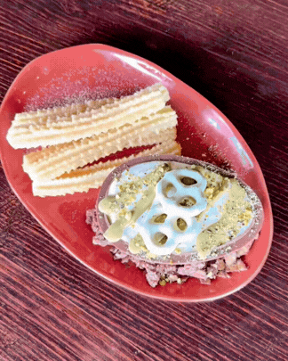 A red plate with kidney-shaped potato chips, a dip with lotus root slices on top, all on a dark wooden surface.