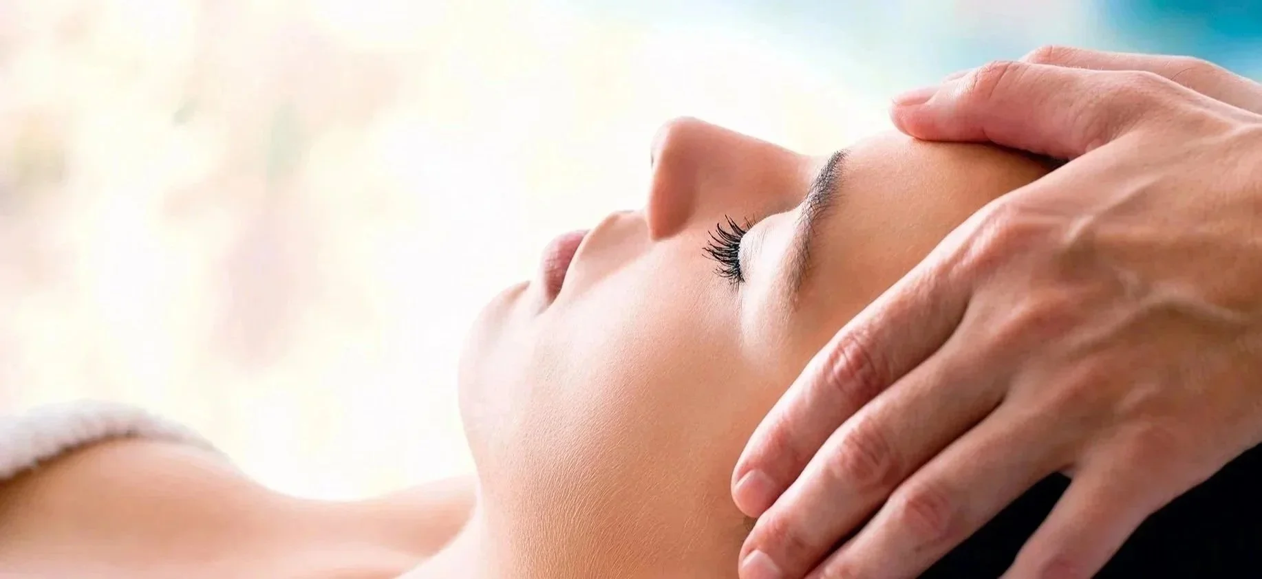 Close-up of a woman receiving a facial massage, eyes closed, with a gentle hand on her forehead.