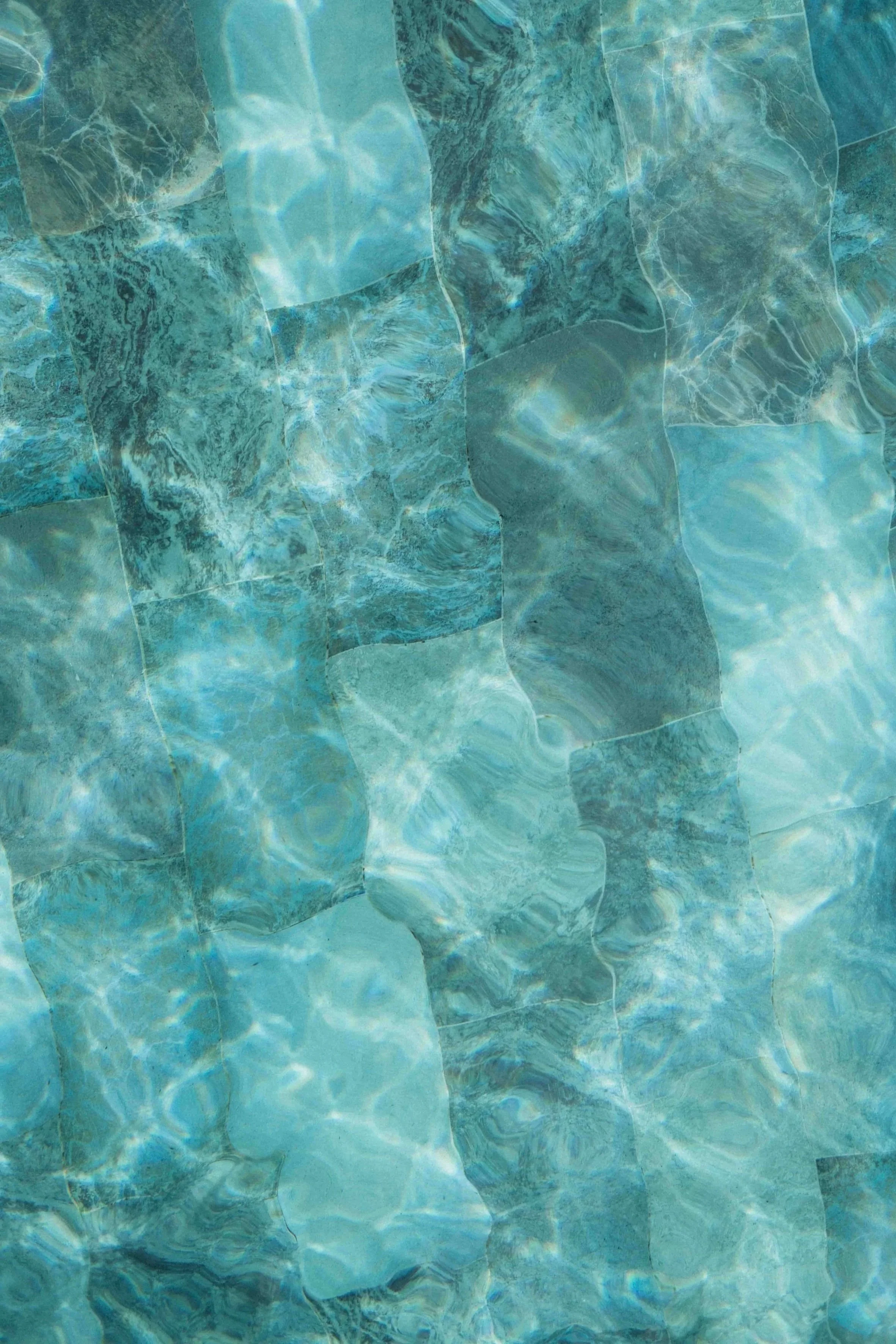 A close-up of a pool floor with blue and green marble-like tiles and water reflections.