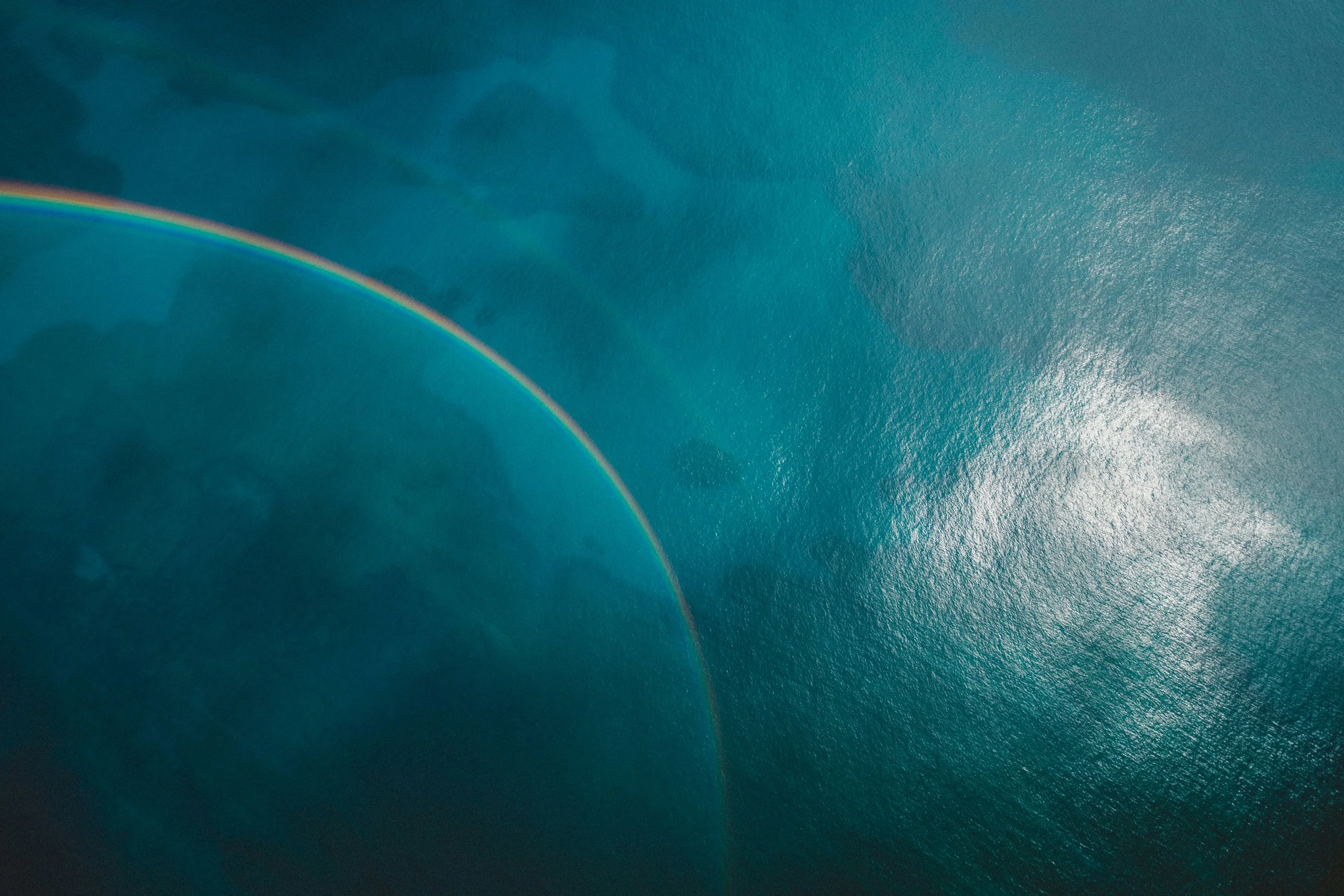 An aerial view of a body of water with a rainbow visible in the upper left portion.