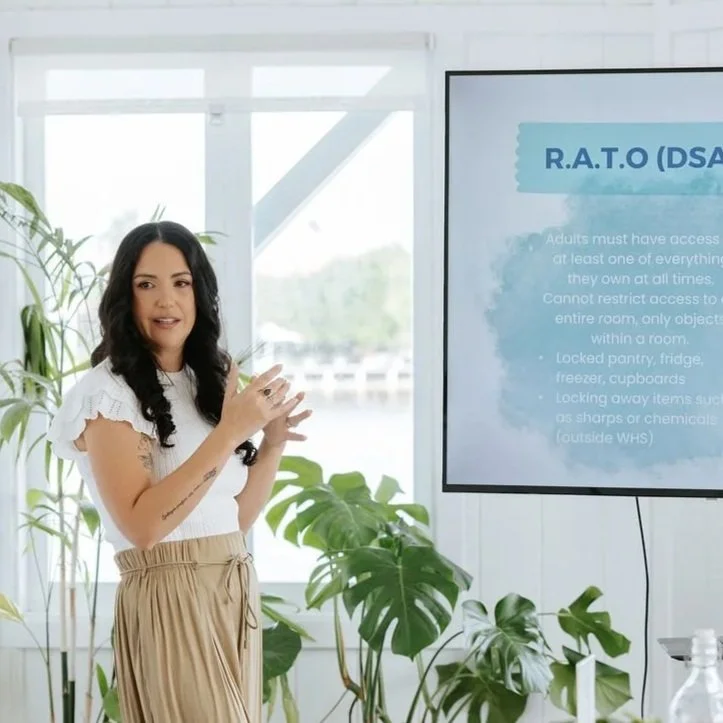 Candice Heffernan giving a presentation in front of a large screen with a slide about R.A.T.O. policy, in a bright room with large windows and green plants.