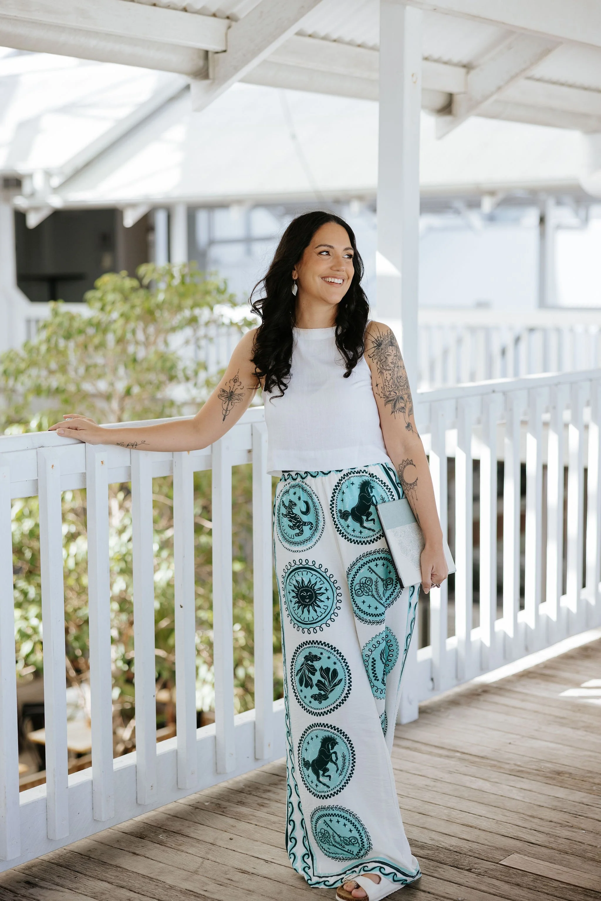 Candice Heffernan smiling while leaning on a white railing on a porch or balcony during daytime.