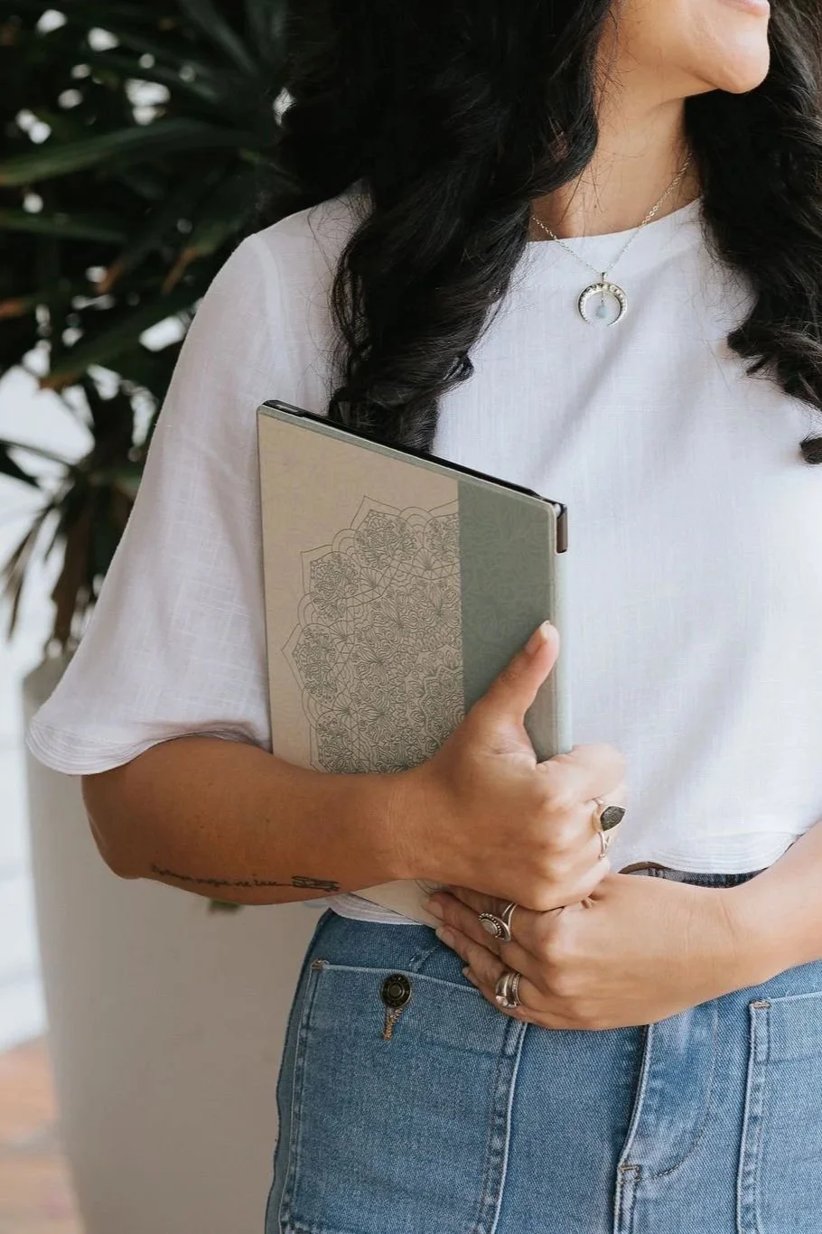 Candice Heffernan wearing a white top and blue jeans, holding a planner or notebook.