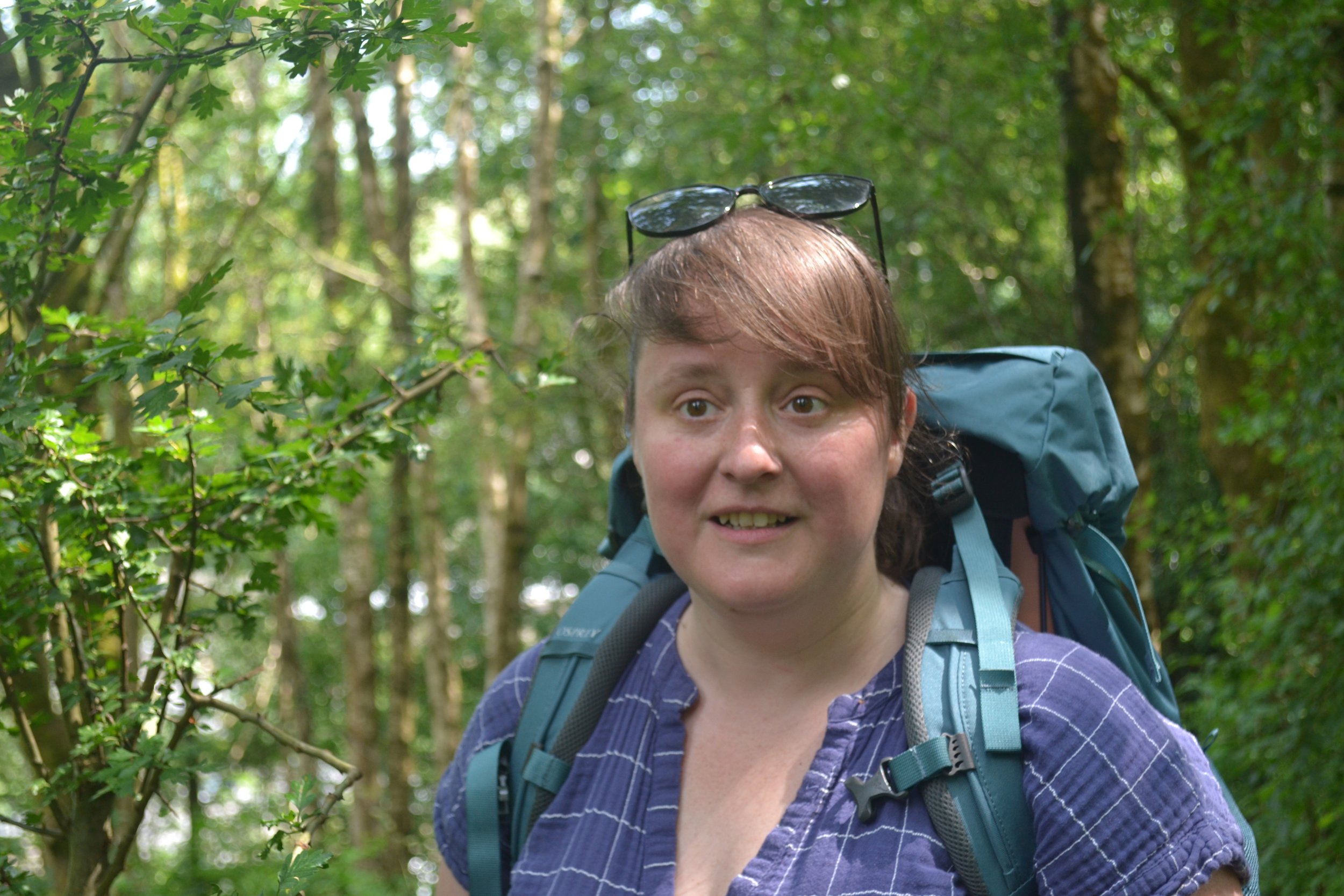 a woman carrying a rucksack, standing in a woodland on a sunny day