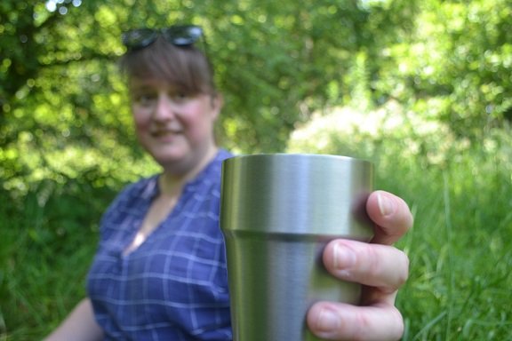 A happy woman holding out a brushed metal beaker or cup