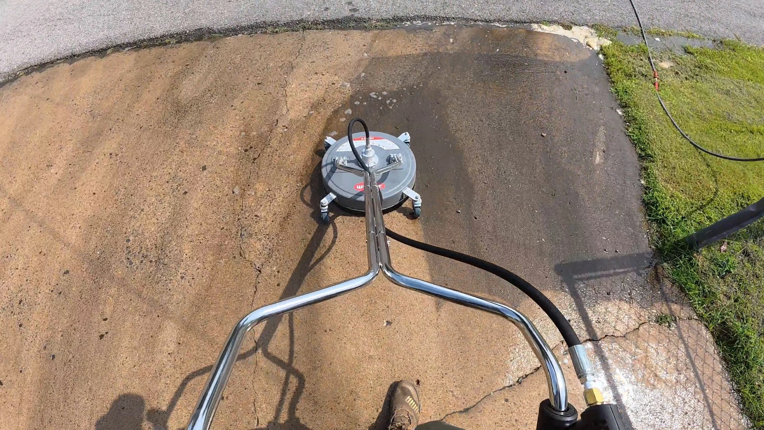 Top-down view of a person pushing a concrete surface grinding machine with a round grinding pad, on a patch of concrete next to a grassy area and a sidewalk in Checotah Oklahoma.
