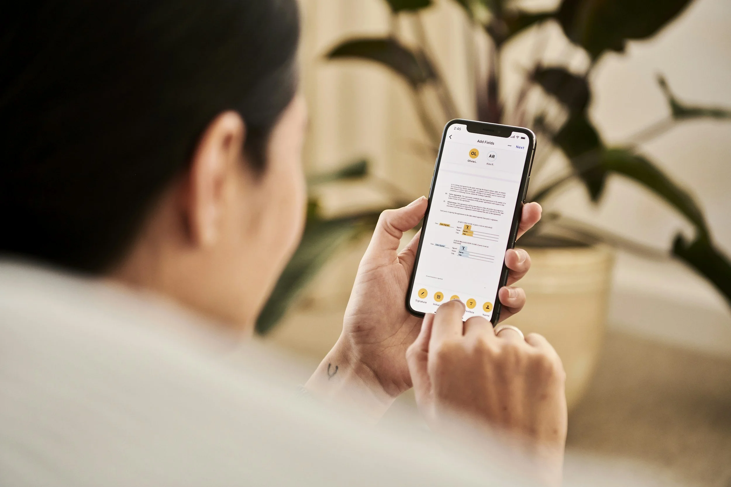 A person holding a smartphone with a document editing app open, with a plant in the background.