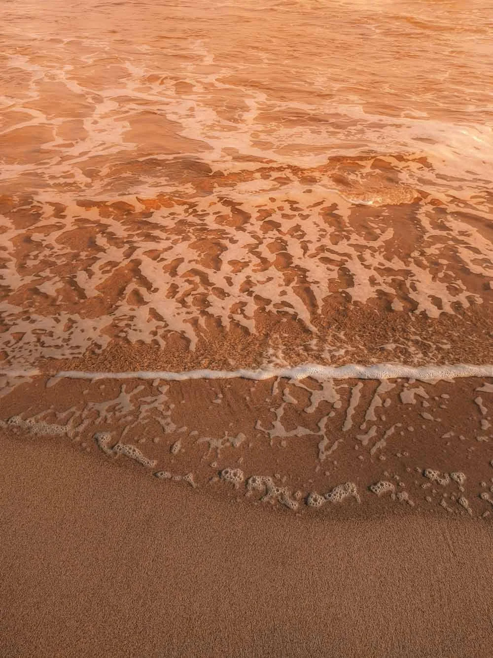 Nahaufnahme eines Strandes mit Sand, Wasser und kleinen Wellen.