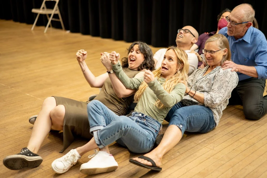 Five improv students riding a roller coaster in three rows, fists clenched and laughing.