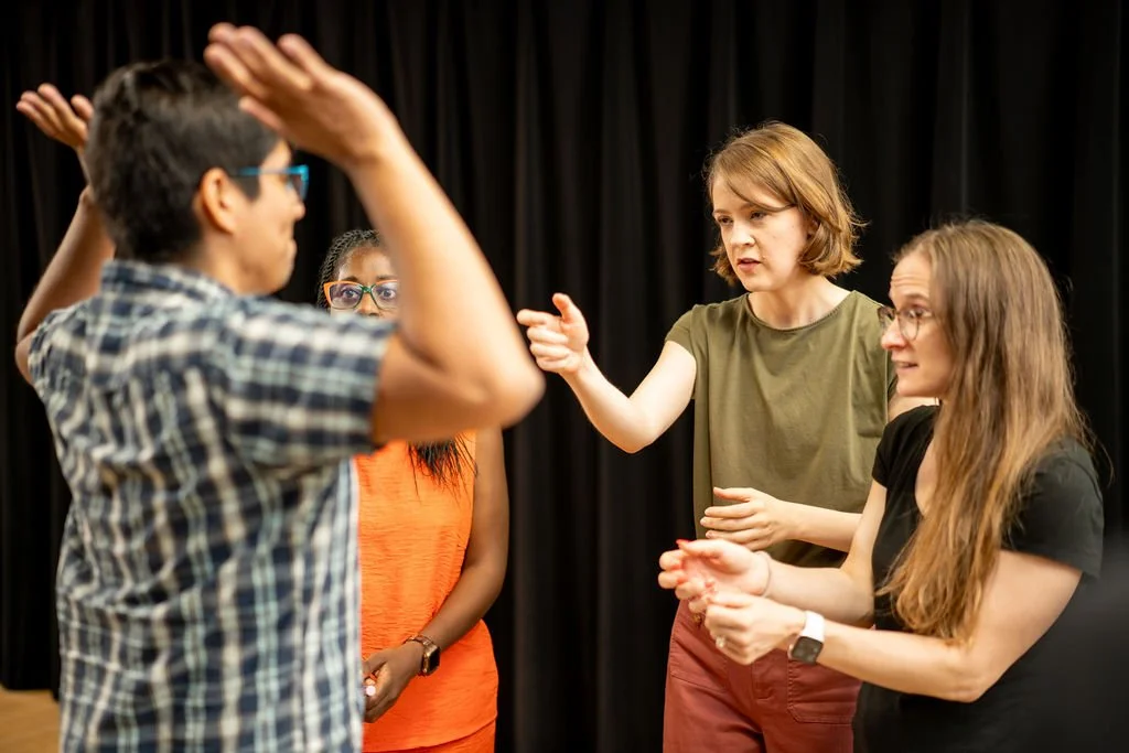 Four improv students playing a scene in which two of them rob the other two at gunpoint.