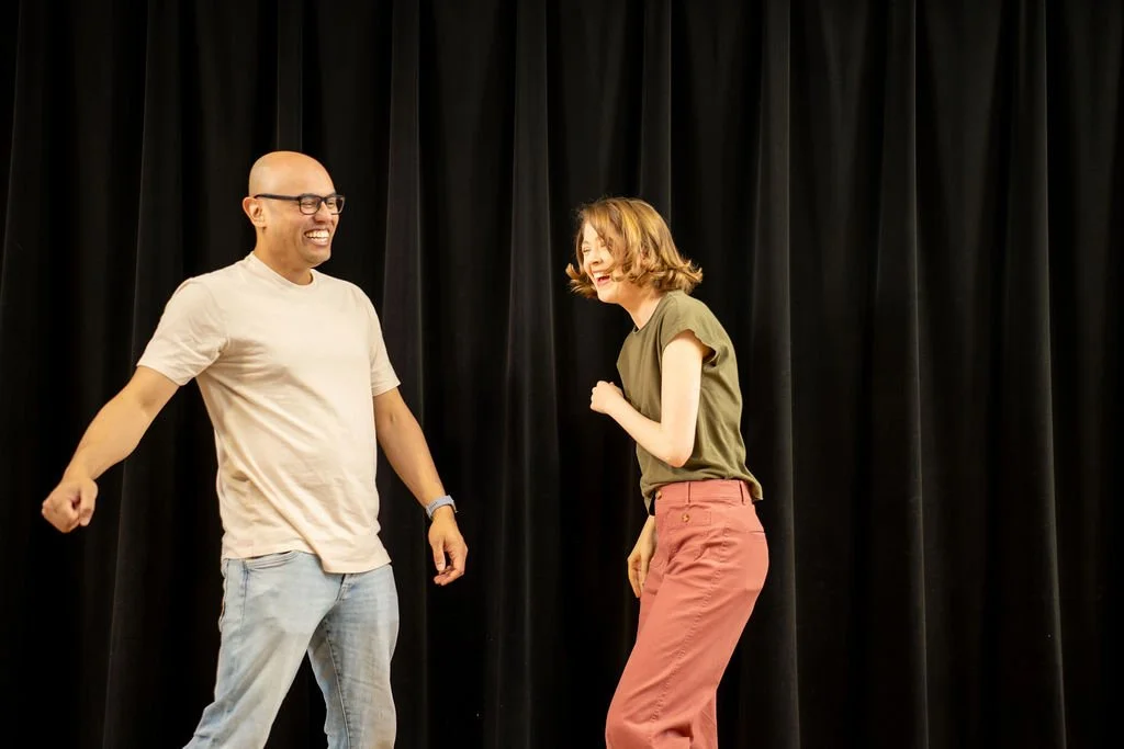 Two students grinning mid-scene in Gary Jacobs's improv class at Bethesda Improv Theater, one striding toward the other.
