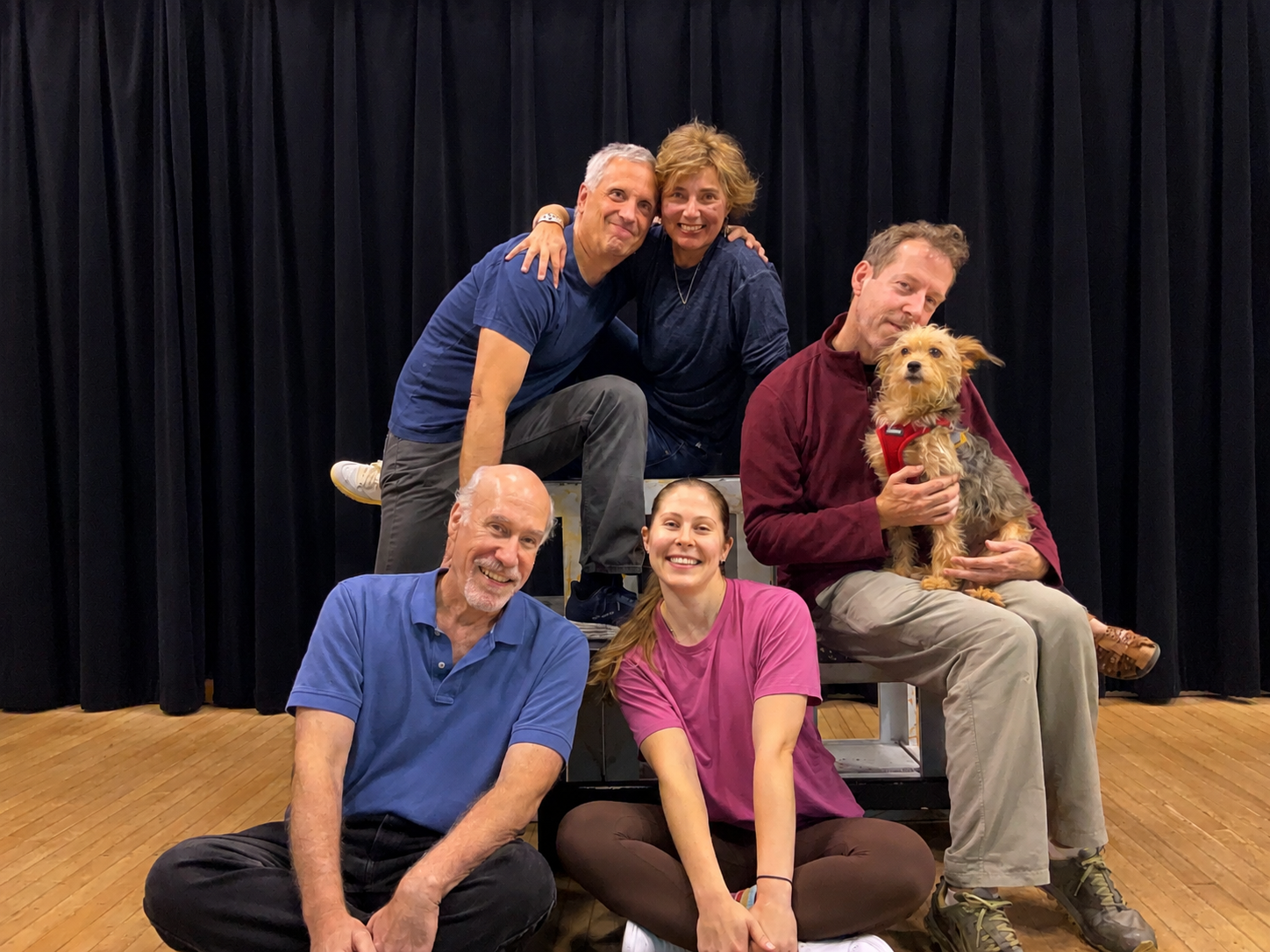 The Precipice Improv Theater troupe, posed with their dog in front of black stage curtains at Imagination Stage in Bethesda, MD.