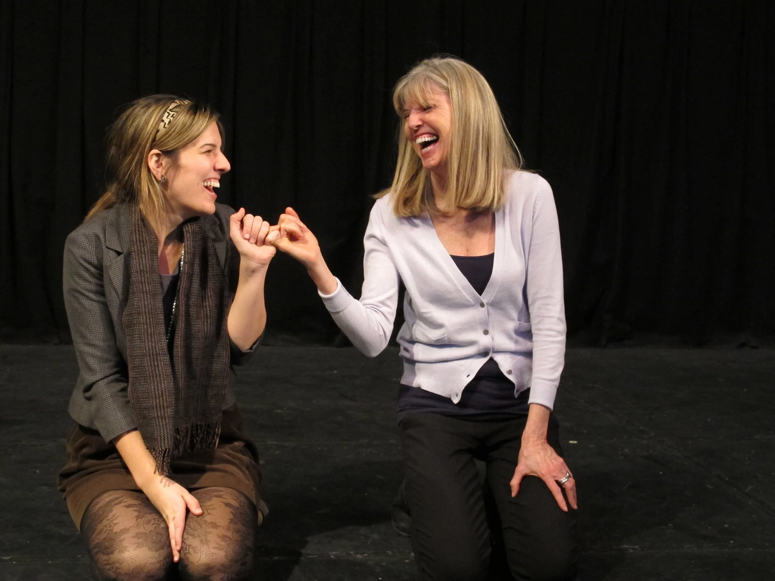 Two improvisers laughing mid-scene during a Precipice Improv Theater class in Bethesda, MD.