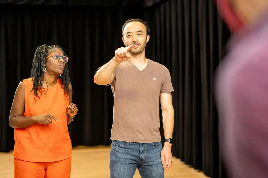 An improv student performing a scene in which he shows another improv student a spot on an imaginary bulletin board by pointing to it with his index finger.