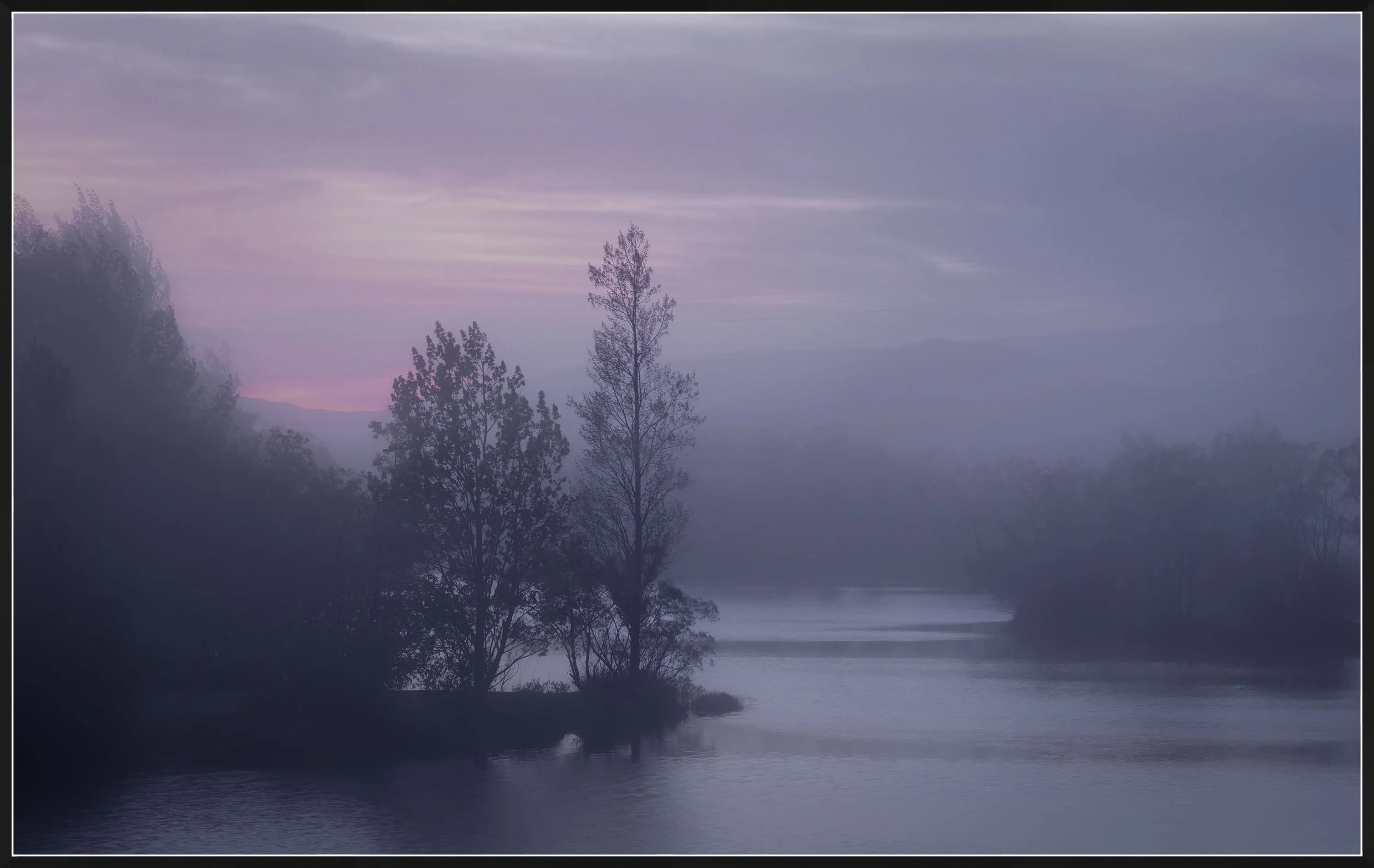 A peaceful river scene at dawn with mist rising above the water, silhouetted trees along the riverbank, and a soft purple and pink sky.