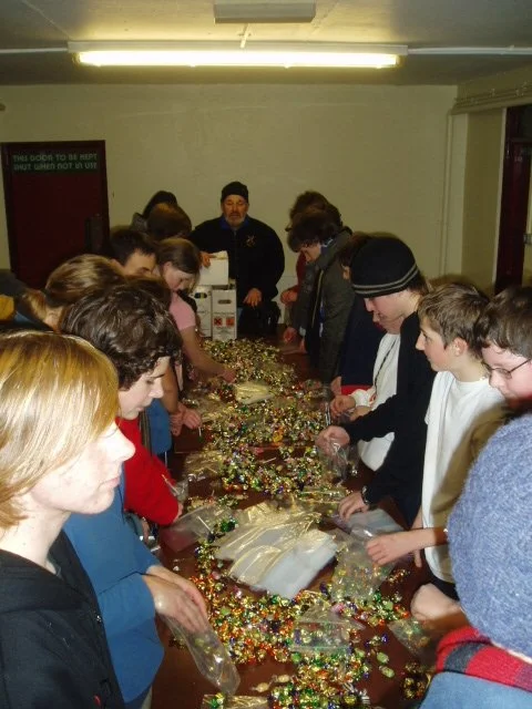 Group of people gathered around a table decorating with colorful beads and ornaments.