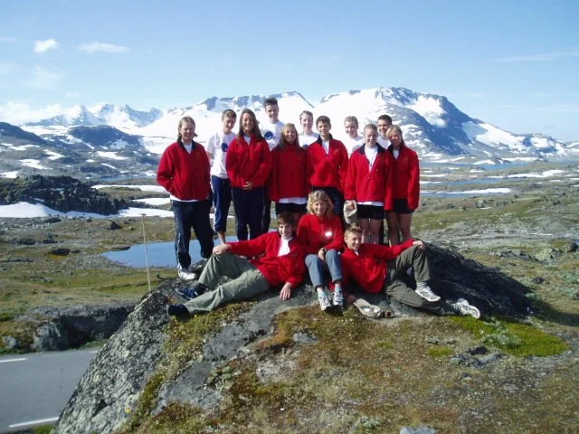 Group of young people in red jackets on a rock in a mountainous landscape with snow-capped peaks.