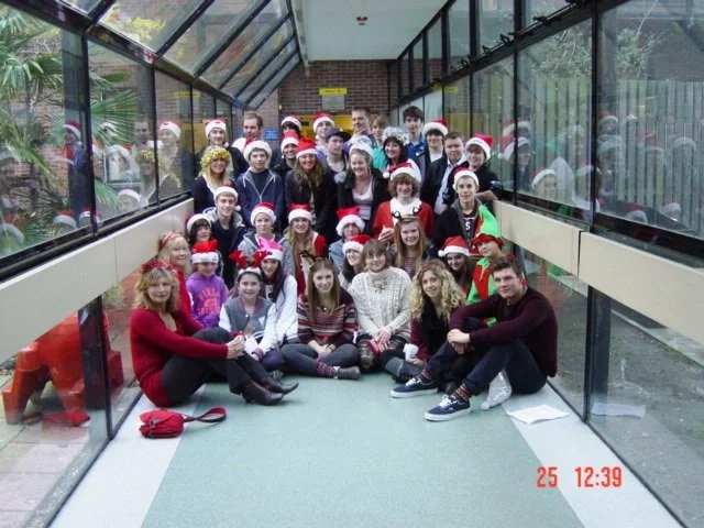 Group of children and adults wearing Santa hats in a glass corridor