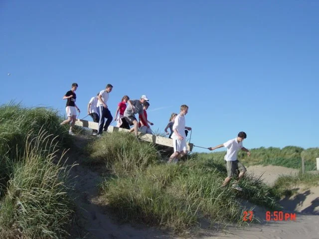 A group of children climbing up a grassy sand dune near the beach on a sunny day.