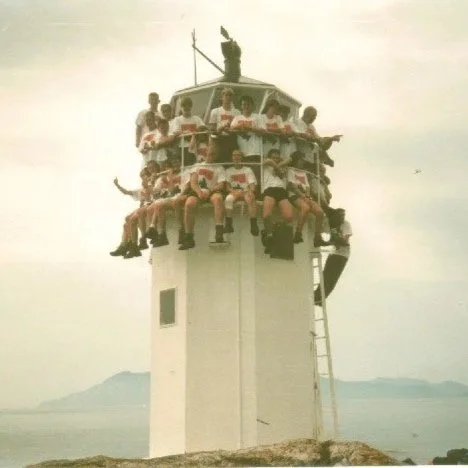 Group of people sitting around the top of a lighthouse, with a single person standing at the very top.
