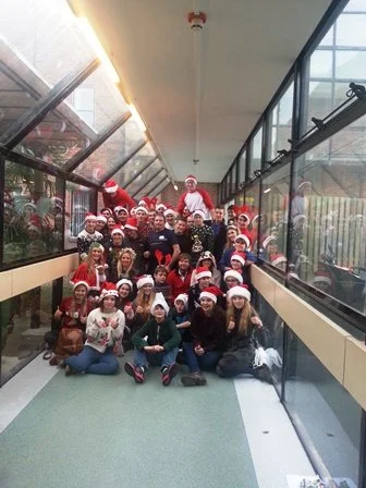 Group of people wearing Santa hats posing in a glass hallway.