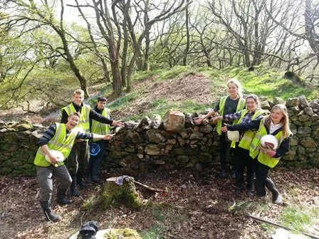 Group of young people in high-visibility vests at an outdoor site, working on a stone wall repair.