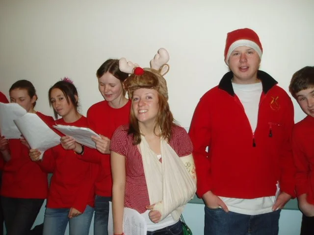 Group of teenagers dressed in red for a holiday celebration, with one girl wearing reindeer antlers headband and a girl in front with a cream arm sling.
