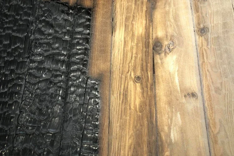 Close-up of a wooden surface with one part burned and blackened, showing charred and cracked wood alongside unburned, natural-colored wood.