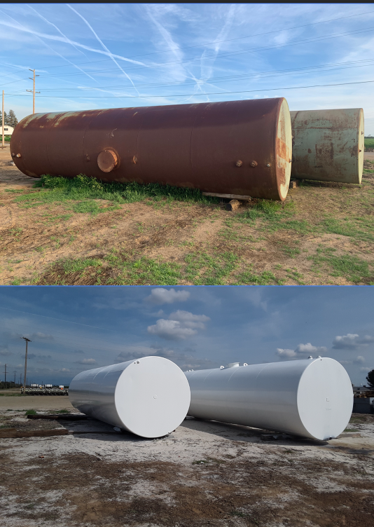 Two large horizontal storage tanks, one rusted and weathered, and the other freshly painted white, situated outdoors on a dirt lot under partly cloudy skies.