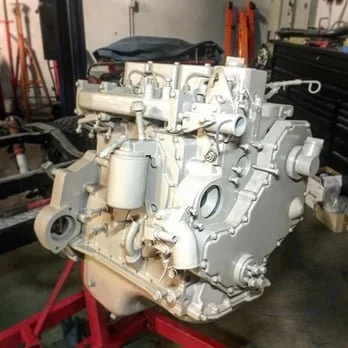 Large, white internal combustion engine with various pipes and components mounted on a red stand in a workshop.