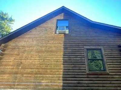 The side of a two-story house showing a transition from light-colored wood siding on the left to darker wood siding on the right, with two windows visible.