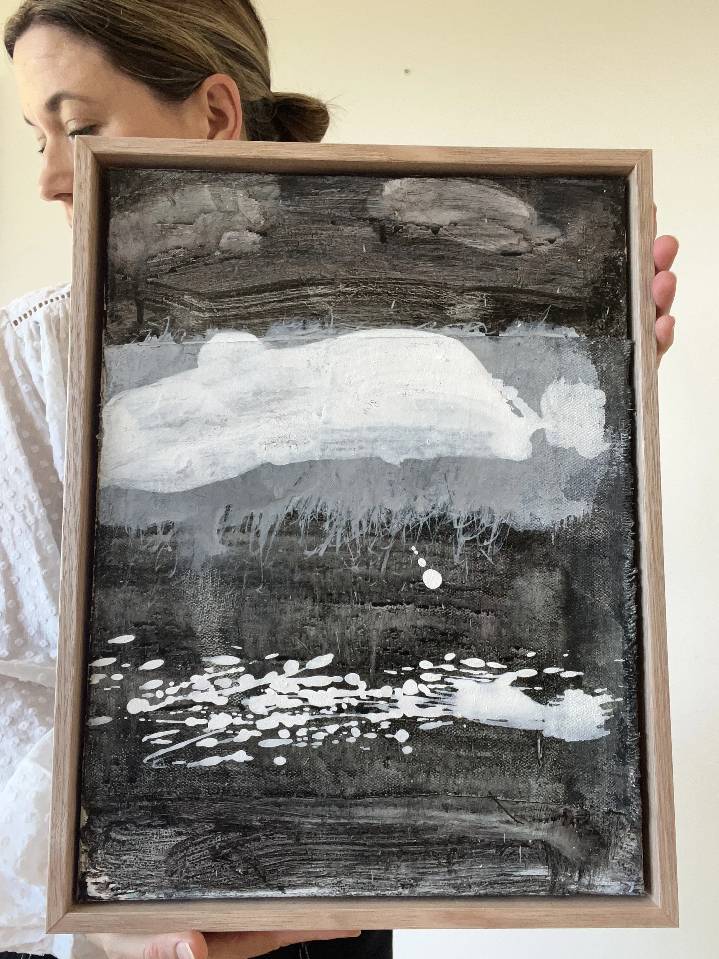 A woman holding a framed black-and-white painting of a seascape with waves and a cloudy sky.