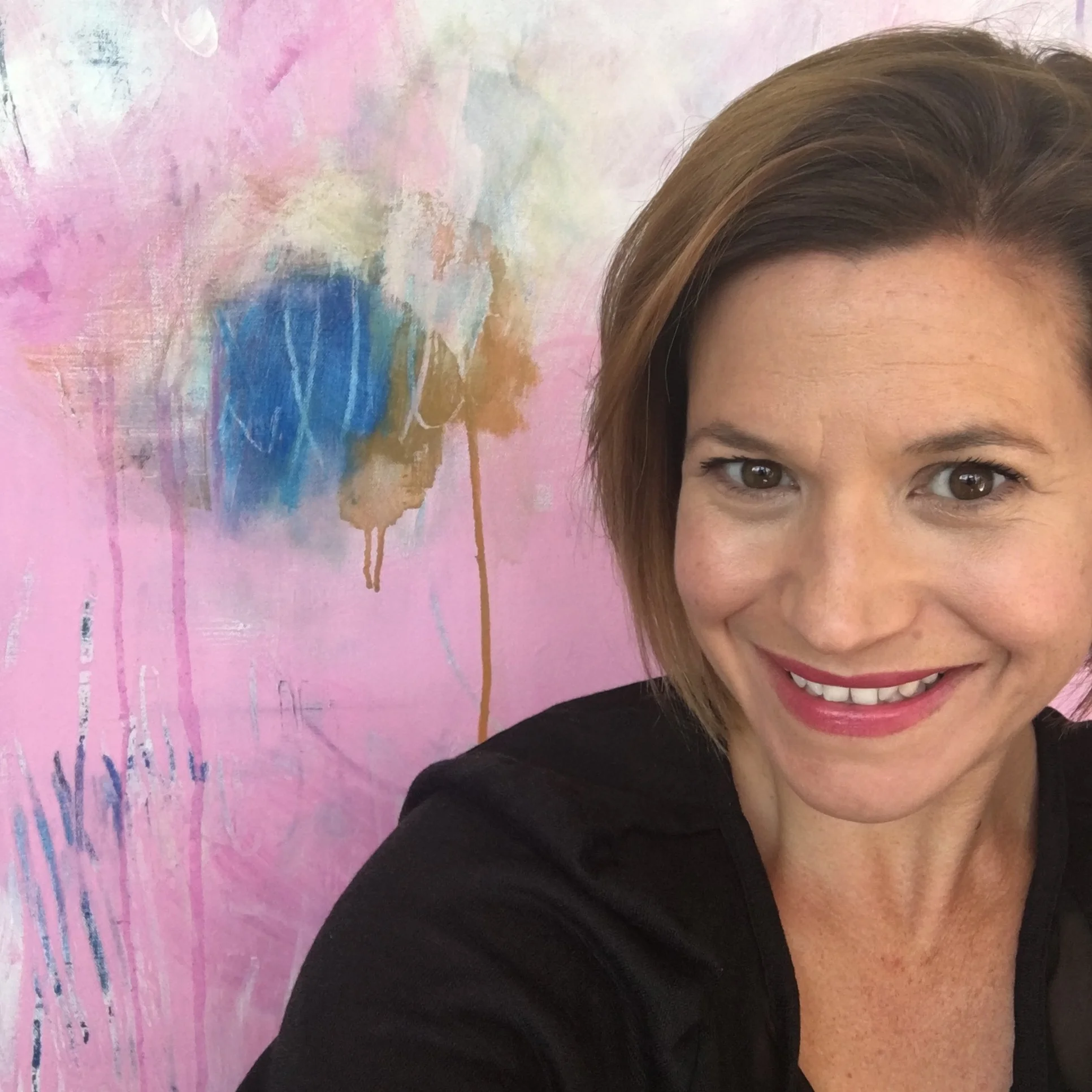 Smiling woman with brown hair and light skin in front of pink and pastel-colored abstract background.