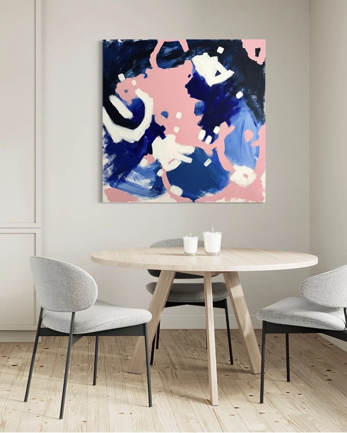 Abstract painting with dark blue, light blue, white, and pink colors hanging on a light gray wall above a round wooden table with three white candles, surrounded by four light gray chairs in a modern dining room.