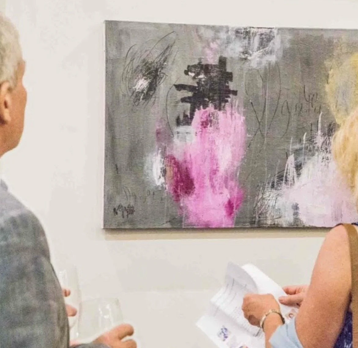 People at an art gallery looking at an abstract painting with pink, black, and gray colors.