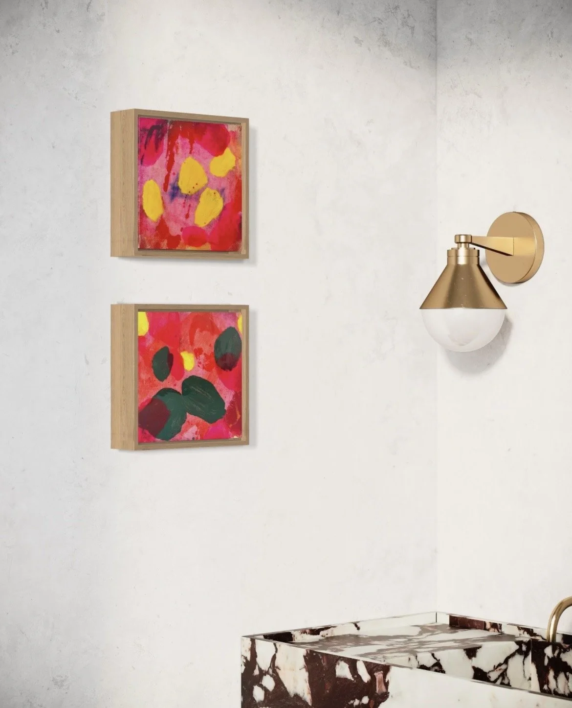 Two colorful abstract paintings with bright pink, yellow, green, and dark red colors hanging on a white wall. A brass wall sconce with a white glass shade is mounted beside the paintings. A black and white marble countertop is partially visible at th