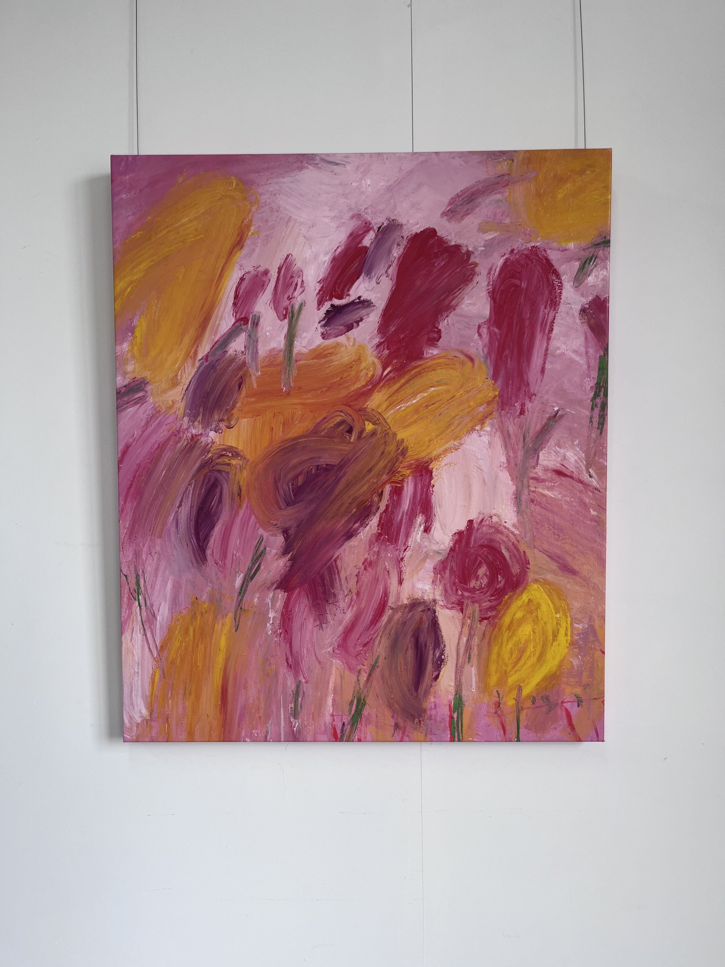 Abstract painting with bold brushstrokes in shades of pink, purple, orange, yellow, and green on a large canvas, displayed against a blank white wall.