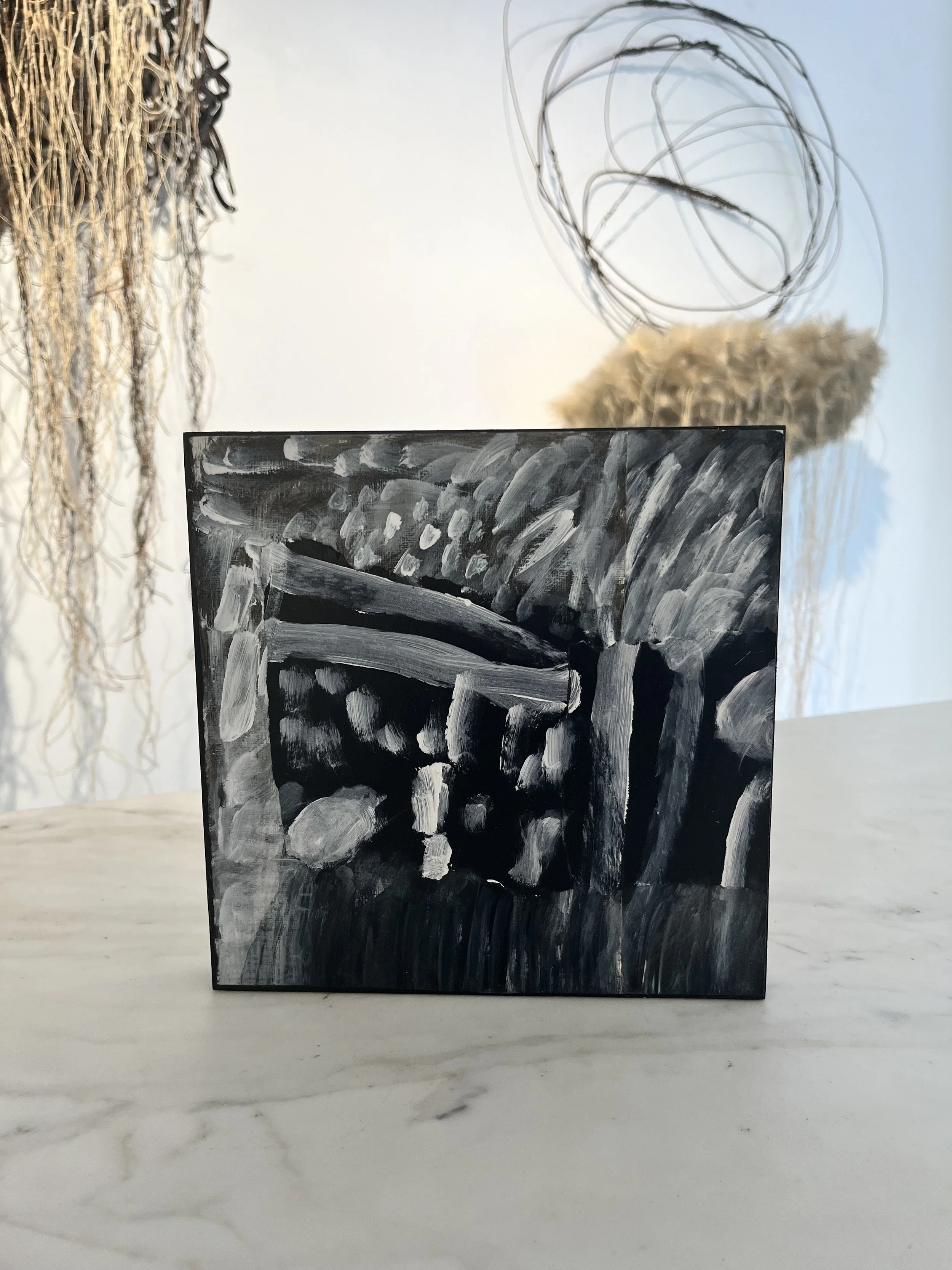 Black and white abstract painting with bold brushstrokes, placed on a light-colored marble surface with a faint gray veining.