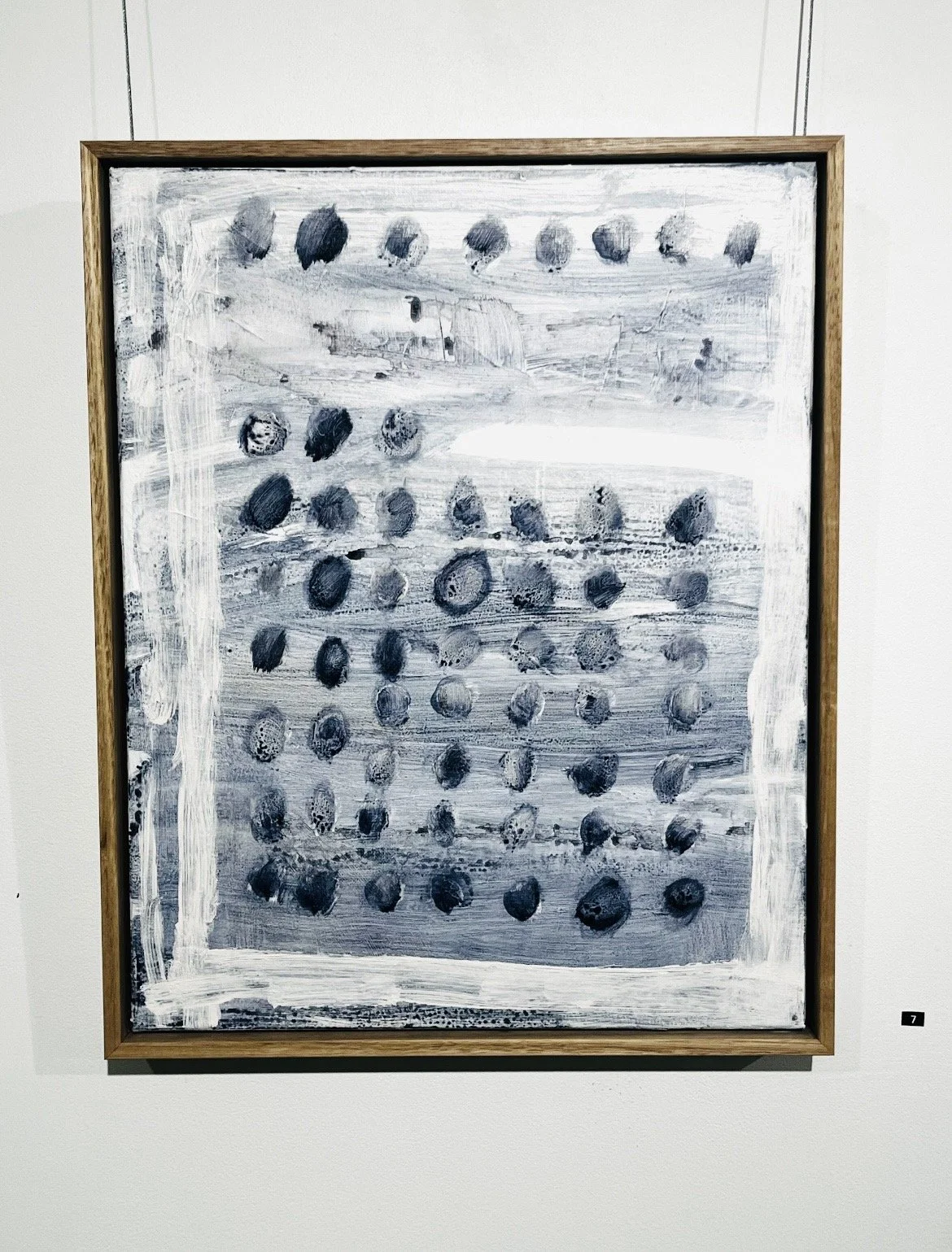 A black and white abstract painting with numerous circular shapes and textured brushstrokes in a wooden frame.