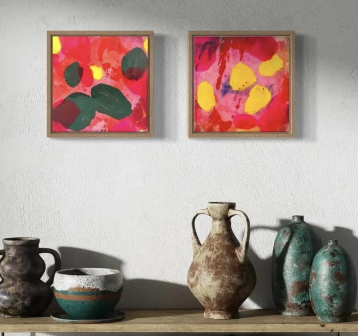 Decorative pottery vases and bowls on a wooden shelf below two colorful abstract paintings on a white wall.