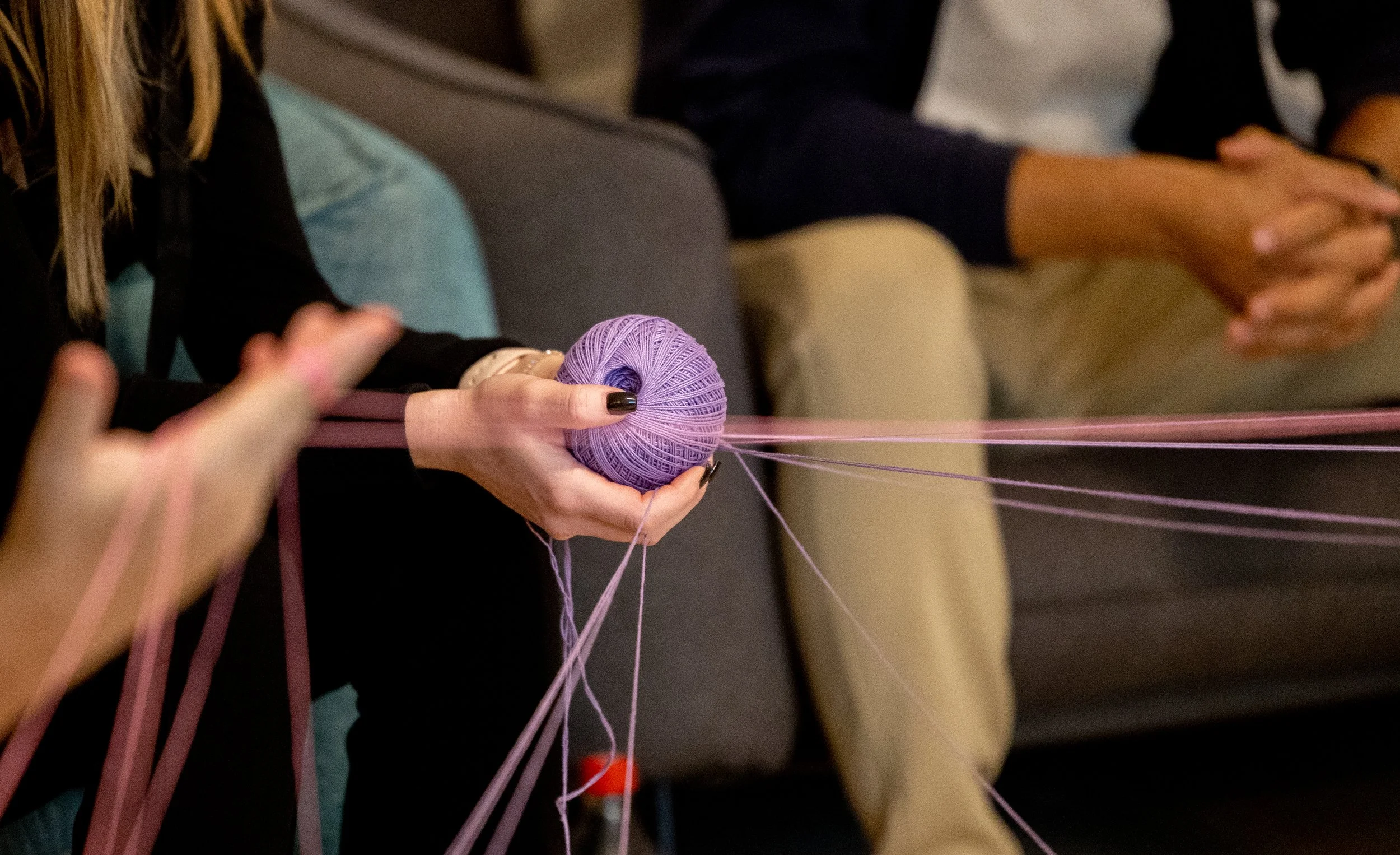 A person holding a purple ball of yarn with pink strings extending from it, in a setting that suggests knitting or crafting.