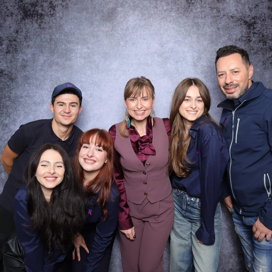 Group of six diverse people smiling and posing together in front of a grey textured background.