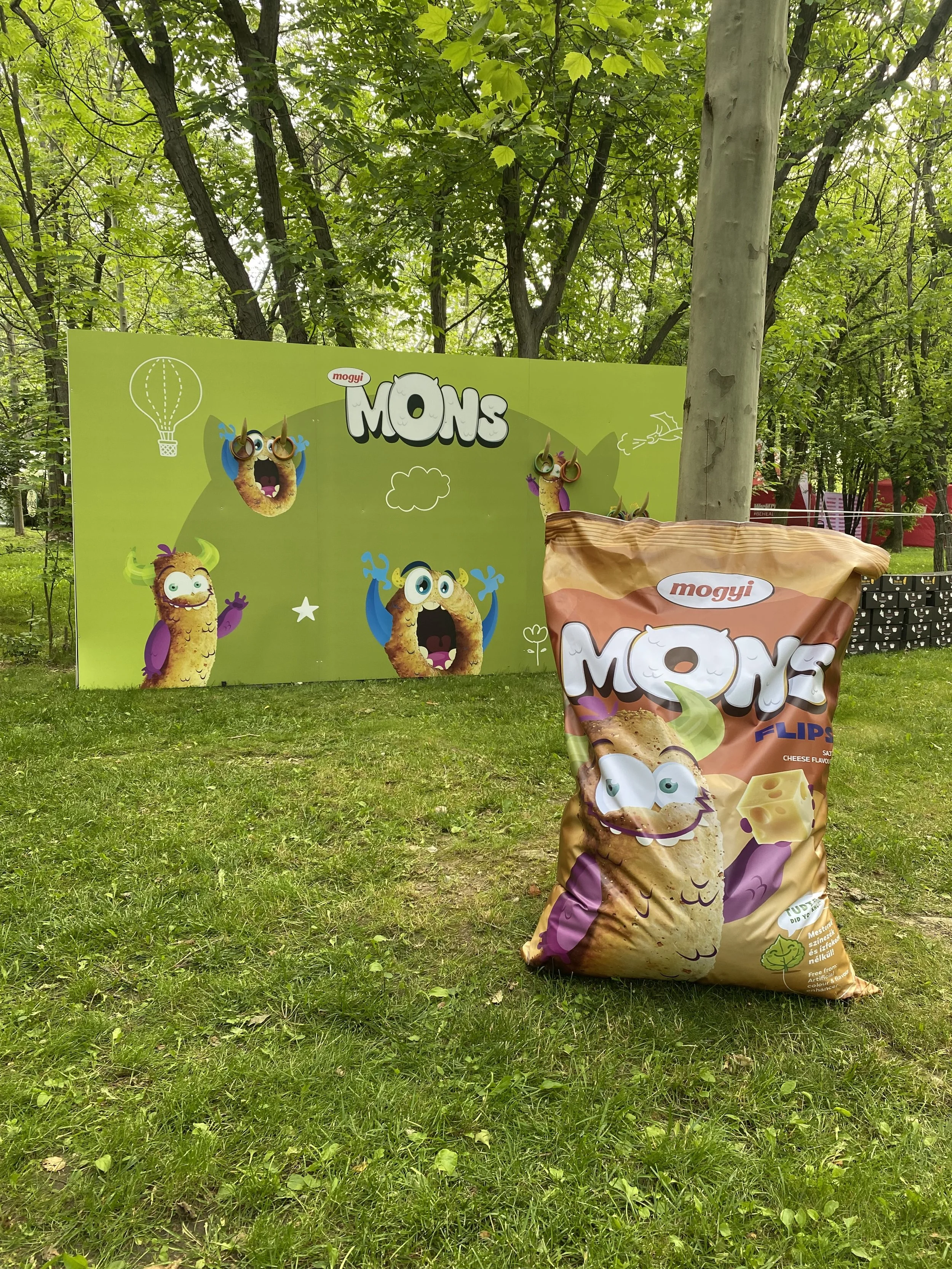 Colorful display of Monster-themed snack packaging outdoors with trees and grass in the background. The packaging features animated monster characters.