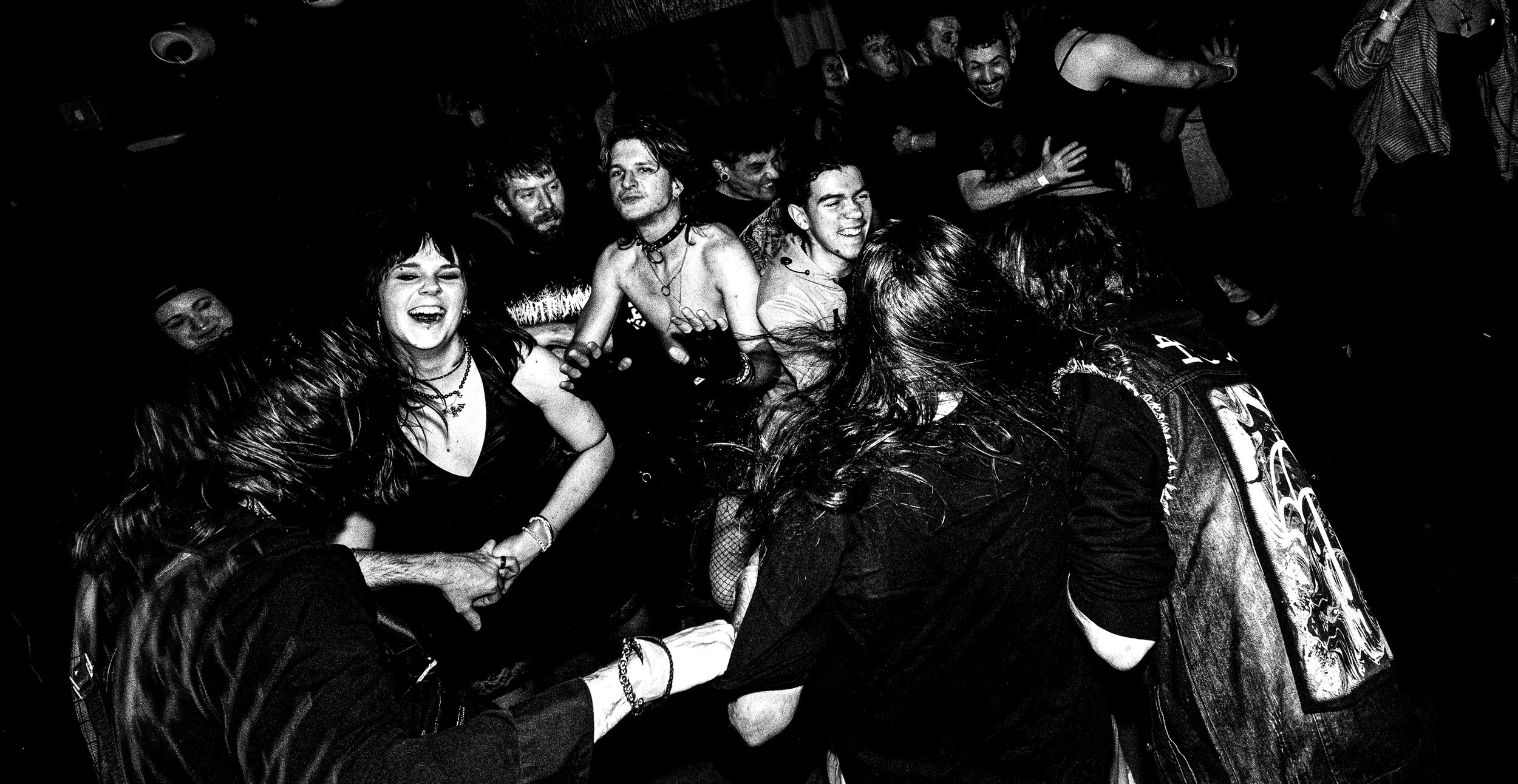 A black and white photograph of a lively concert scene with diverse people enjoying the music. Some are smiling, others are dancing or singing passionately, with energetic expressions and gestures, immersed in the performance.