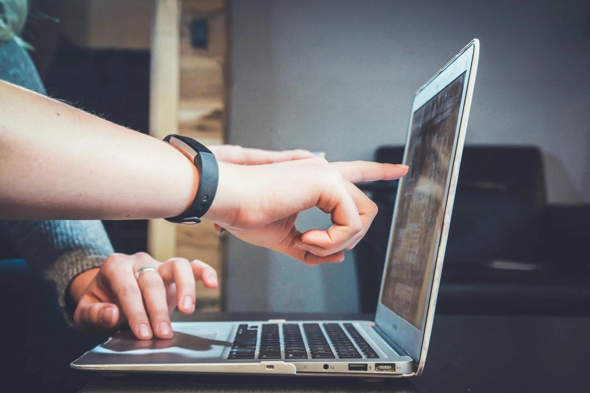 A person with a fitness tracker on their arm working on a silver laptop with a reflective screen.