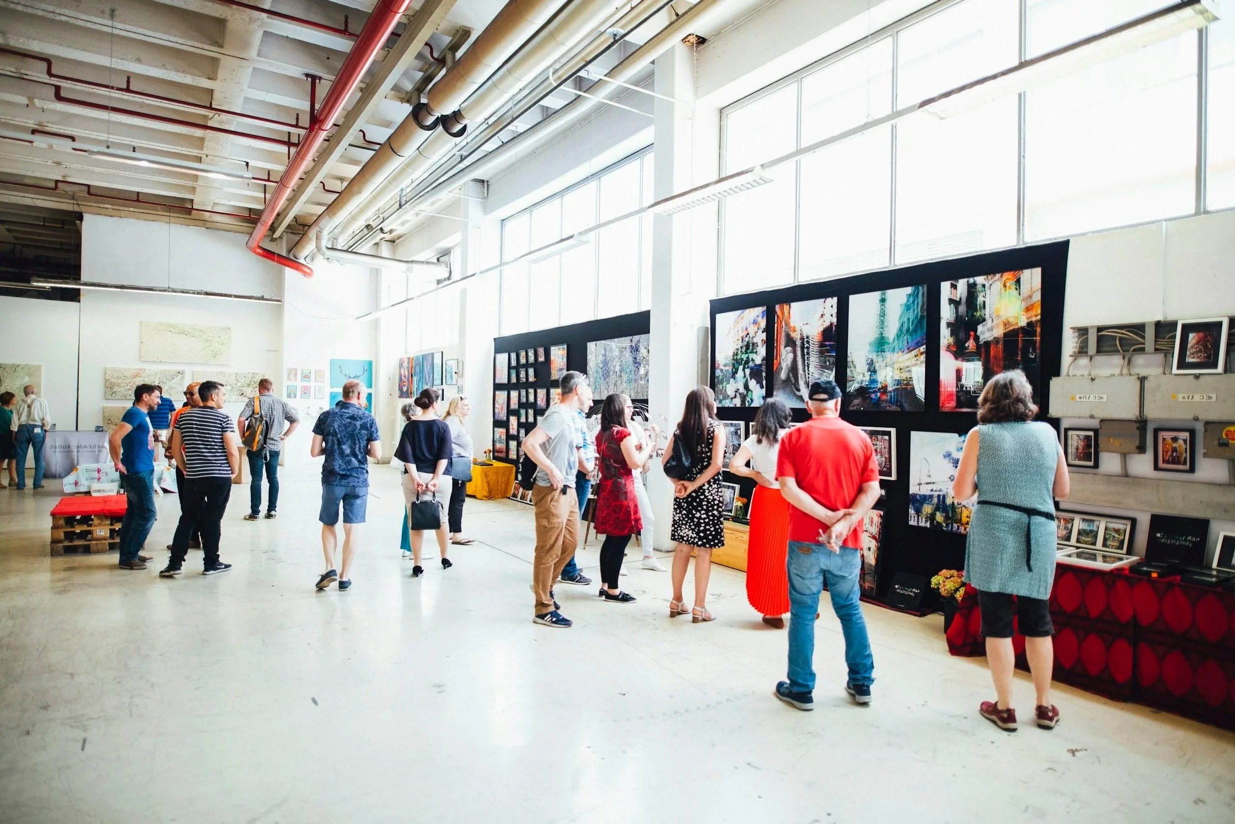 People viewing artworks at an art gallery with paintings displayed on black partitions and walls inside a spacious industrial-style building with large windows.  Heather Ogilvie and The Ogilvie Business School in Dundee, Scotland.