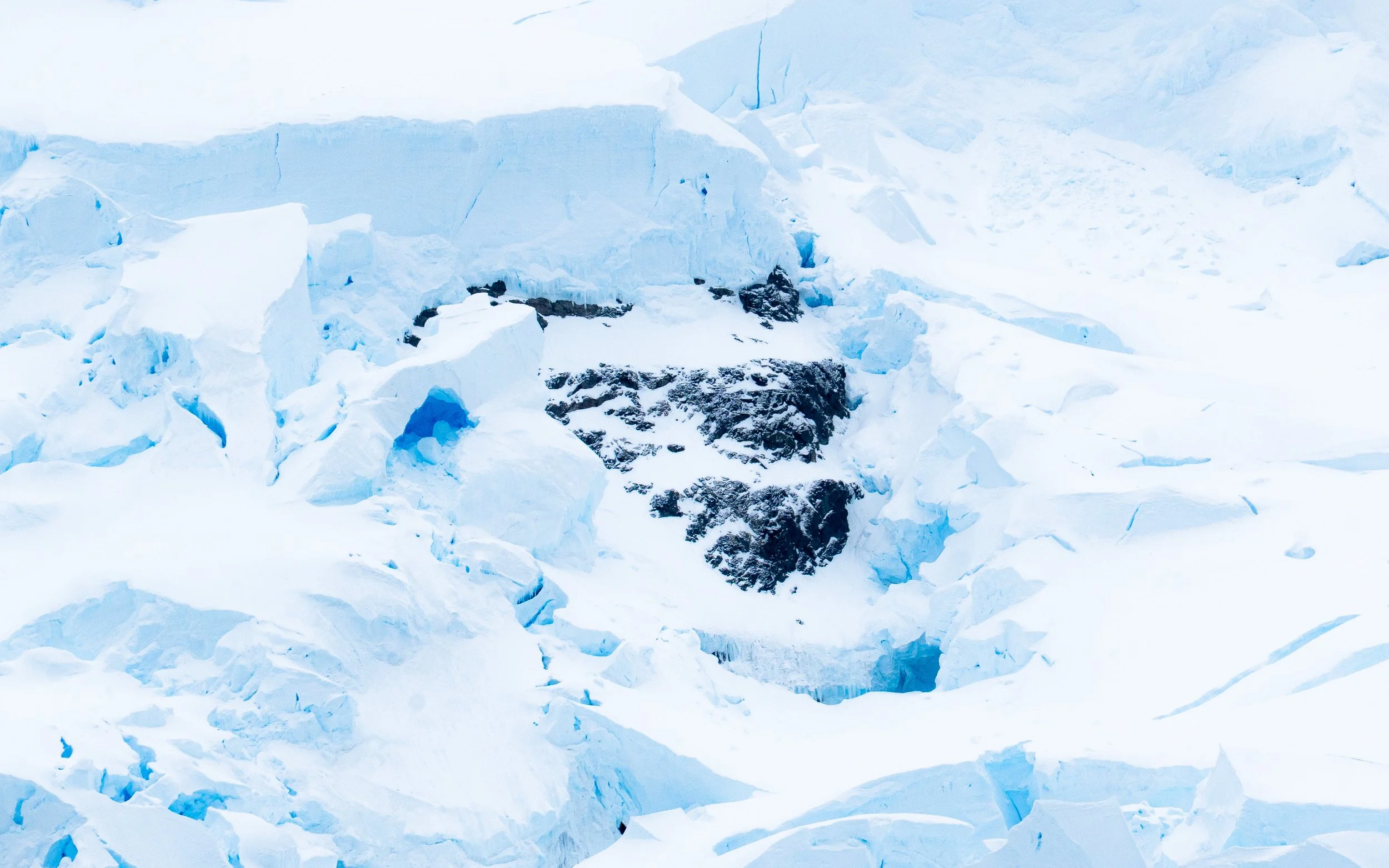 Expansive view of a glacial ice formation with blue and white ice and some dark patches of exposed rock.