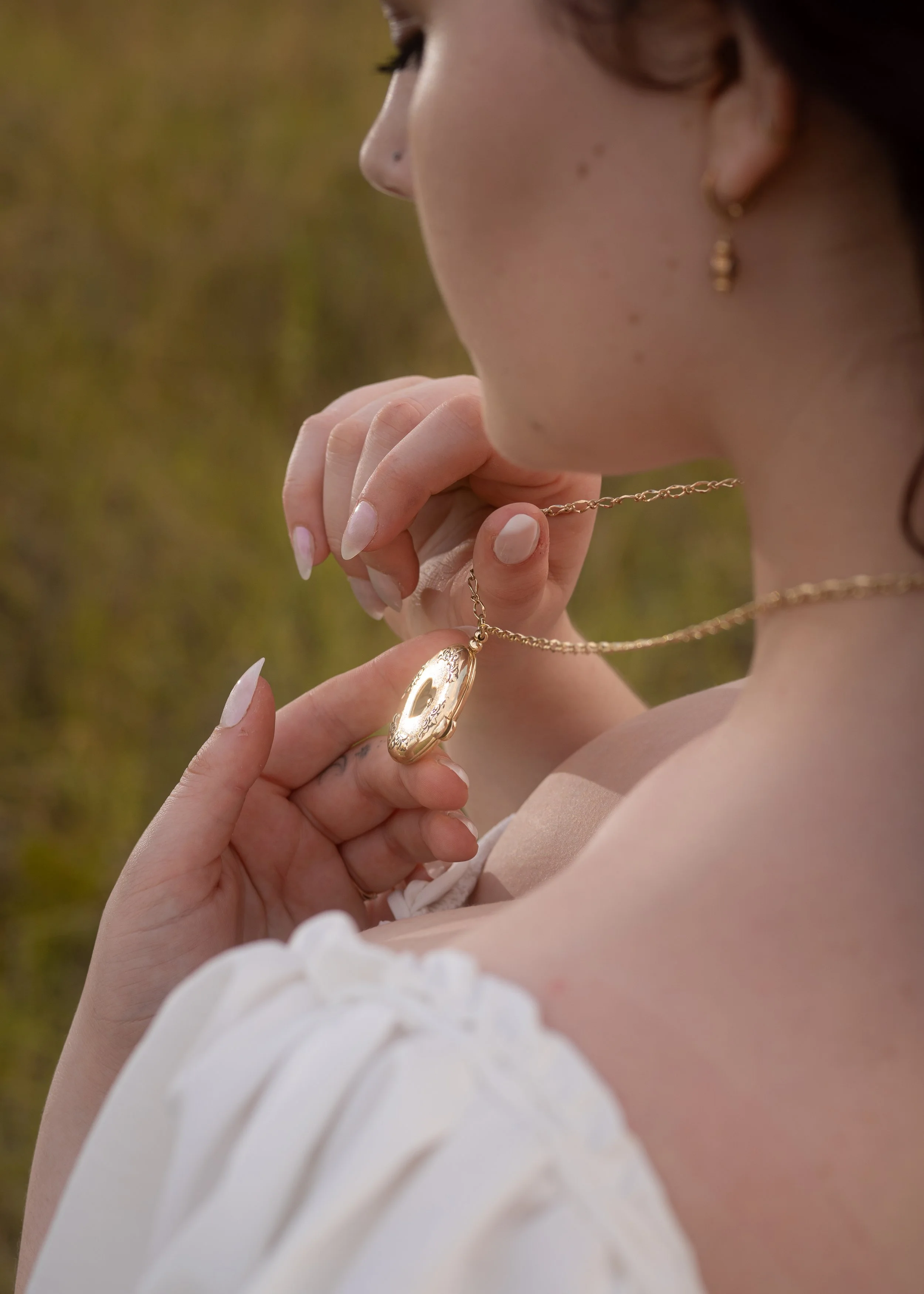 Close-up of a woman with earrings and necklaces, holding jewelry with her hand, outdoors during daytime.