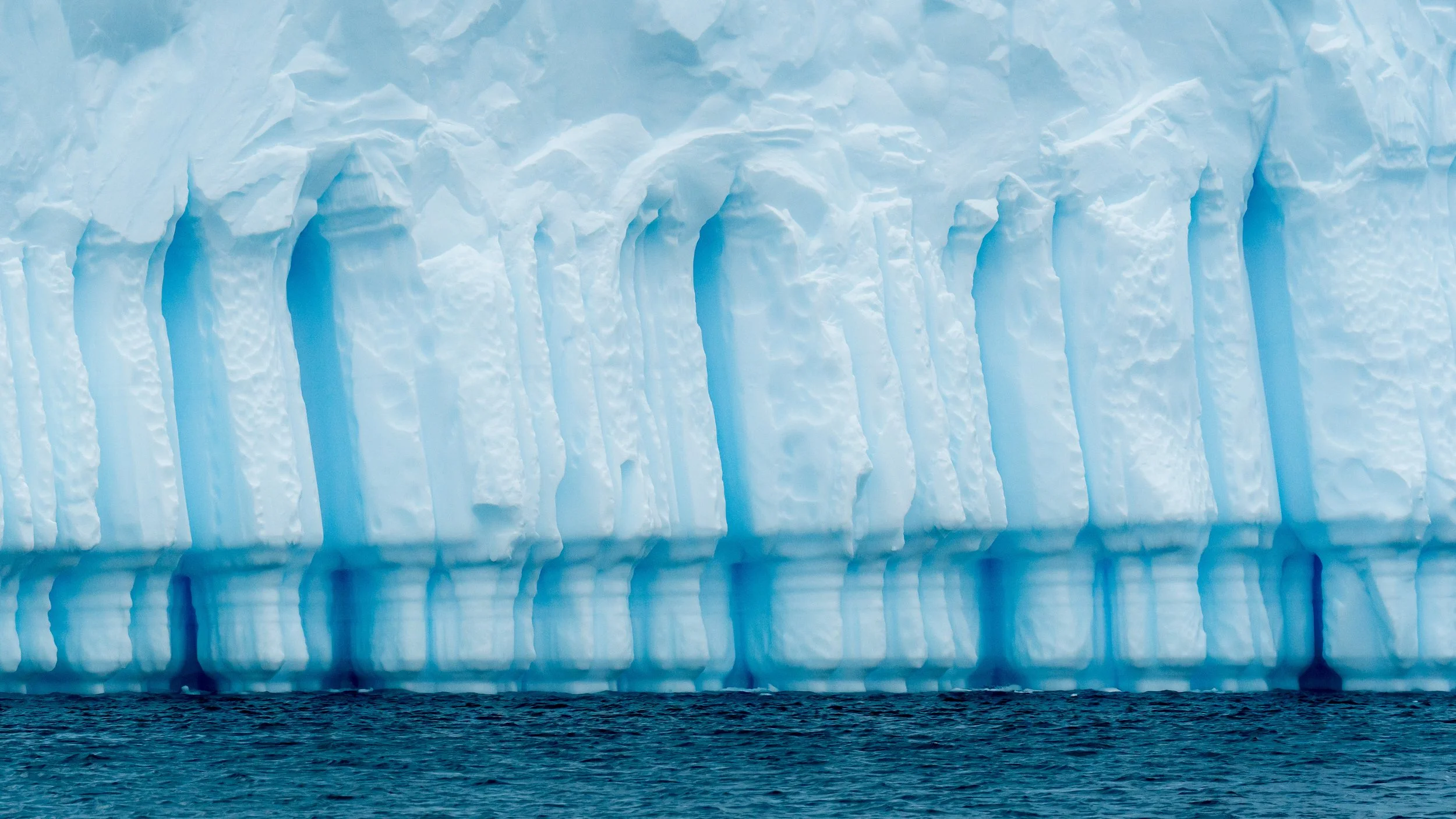 A large glacier with icy blue and white layers calving into the ocean.